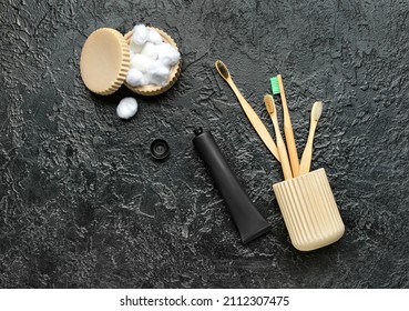 Opened tube with activated carbon toothpaste,  holder with bamboo toothbrushes and cotton balls on dark background