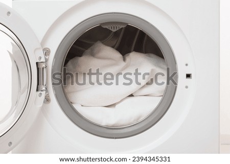 Opened washing machine full of white clothes. Closeup. Front view.