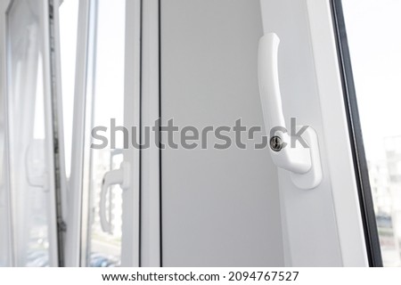 Opened white plastic window handle in upright position close-up. New tilt and turn pvc windows ventilation.
