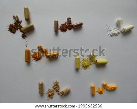 Opened and whole capsules of supplements on white background. From top right to left as follows: resveratrol, grape seed extract (OPC), vitamin C, turmeric (curcuma longa), quercetin, reishi, coenzyme