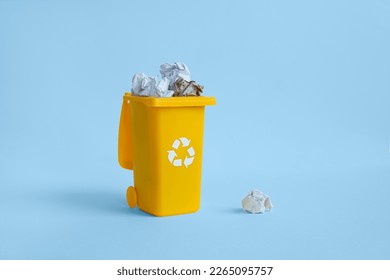 Opened yellow container for paper garbage collection with crumpled paper inside, isolated on the blue background with copy space, waste recycling concept