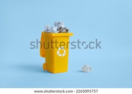 Opened yellow container for paper garbage collection with crumpled paper inside, isolated on the blue background with copy space, waste recycling concept