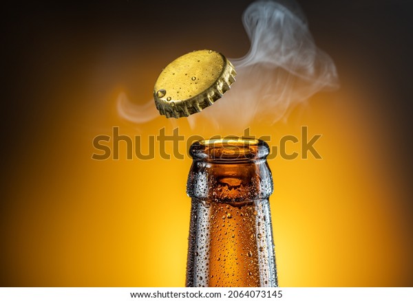 Opening of cold beer\
bottle - gas output and bottle cap in the air. Isolated on a yellow\
background.