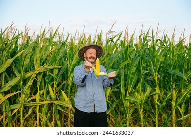 Opening a corn in hands, elderly farmer worker stands in field, glows happiness looking at camera. Sunny weather, large corn field around, clear sky. Copy space. - Powered by Shutterstock