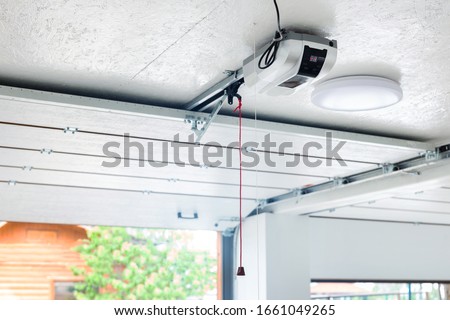 Opening door and automatic garage door opener electric engine gear mounted on ceiling with emergency cord. Double place empty garage interior with rolling entrance gate