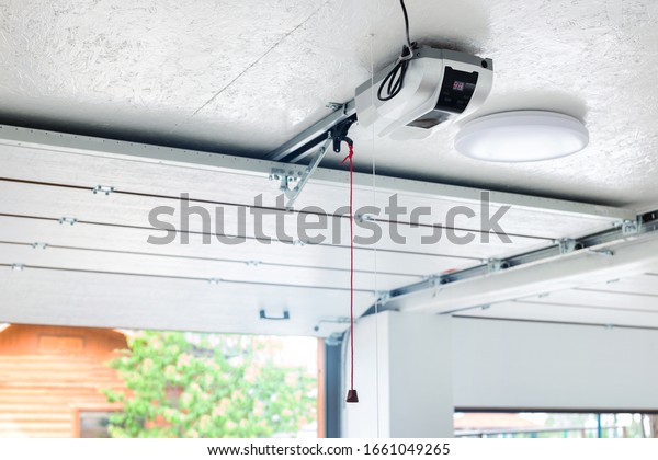 Opening door and automatic\
garage door opener electric engine gear mounted on ceiling with\
emergency cord. Double place empty garage interior with rolling\
entrance gate