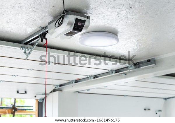 Opening door and automatic\
garage door opener electric engine gear mounted on ceiling with\
emergency cord. Double place empty garage interior with rolling\
entrance gate