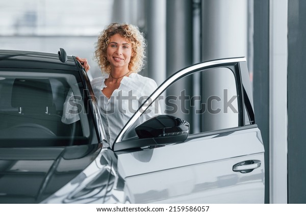 Opening the door. Woman with curly blonde hair\
is in autosalon.