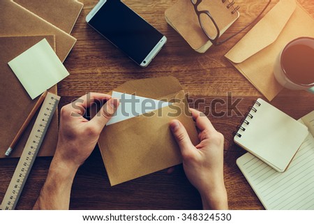 Opening envelope. Close-up top view of male hands opening envelope over wooden desk with different chancellery stuff laying on it