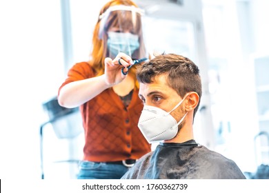 Opening of hairdressing salons after the coronavirus pandemic, covid-19. Security measures, face mask, protective screen, social distance. Hairdresser cutting hair with scissors to a client boy - Powered by Shutterstock