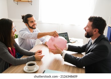 Opening A Savings Account. Happy Couple Putting Their Money On A Piggy Bank And Investing With A Financial Advisor 