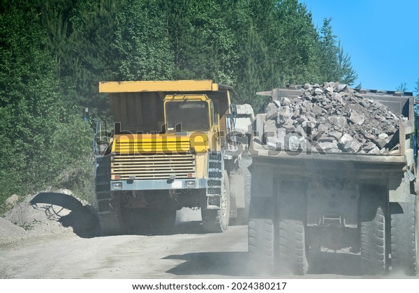 Open-pit operation. Pit\
dump truck, large-capacity dump truck rides on a gravel wet road\
works in a granite quarry (gravel pit). Loaded and empty dump\
trucks, loaded body