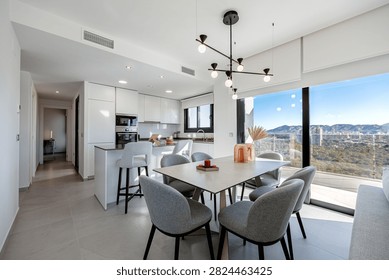 Open-plan kitchen and dining area with a kitchen island, gray dining chairs, pendant lighting, and mountain view through large windows