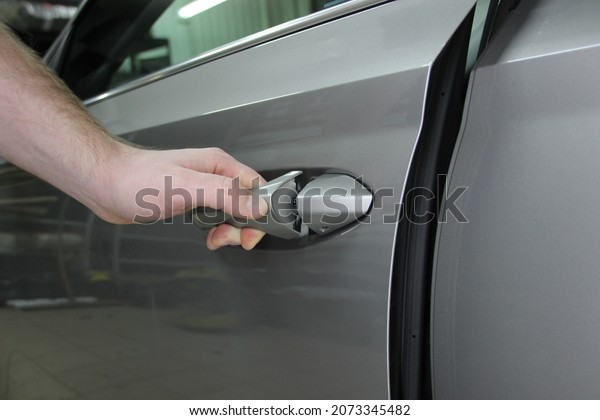 Opens the car door.\
Close-up of a man\'s hand holding the handle of a car. A man opens a\
gray car in close-up.