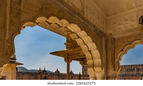 Openwork arched vaults of the palace in the ancient Amber Fort. Against the background of the blue sky - a weathered wall, domes with spires, green mountains. India. Jaipur. - Shutterstock ID 2281623175