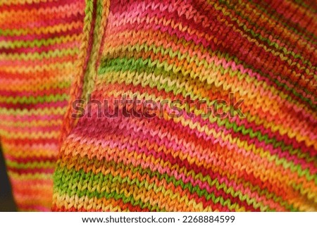 An openwork of colorful woolen scarf. Merino scarf on flat bed knitting machine. Simple Stockinette stitch is one of the most basic knitting patterns. Knit fabric used in scarves.