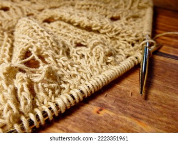Openwork tablecloth in the process of knitting. Knitting needles, loops on knitting needles, knitted fabric, coarse cotton and linen yarn, wooden background