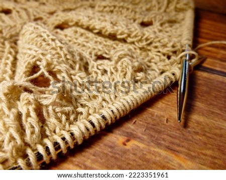 Openwork tablecloth in the process of knitting. Knitting needles, loops on knitting needles, knitted fabric, coarse cotton and linen yarn, wooden background