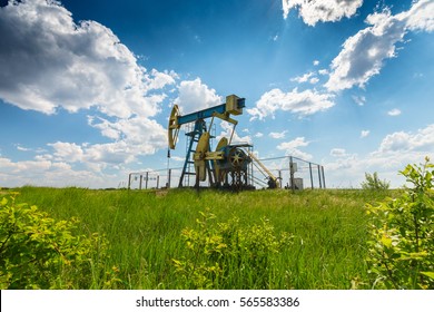 Operating Oil And Gas Well In European Oil Field, Profiled On Blue Sky With Cumulus Clouds, In Spring