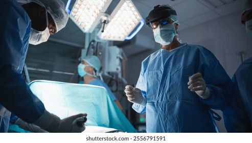 Operating Team Following Directions of a Female Surgeon Using Augmented Reality Headset, Where a Digital Overlay Helping to Streamline the Process During a Medical Operation with a Patient - Powered by Shutterstock