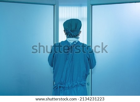 In the operation room of a hospital, a doctor leans on the door.