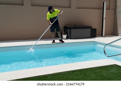 Operator Cleaning A Swimming Pool With A Butterfly Trap, With Artificial Grass And A Shower In The Background.