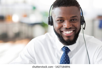 Operator of hot line. Portrait of cheerful african customer service representative with headset in call center, empty space
