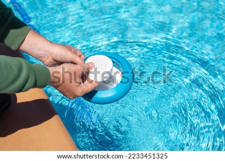 Operator introducing a white chlorine tablet into a floating dispenser in the pool at home in summer for disinfection and maintaining the proper ph for swimming in the pool during the summer