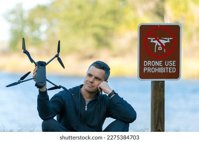 Operator is preparing to fly his quadcopter in national park no drone area. Man unlawfully using his UAV near restriction notice sign
