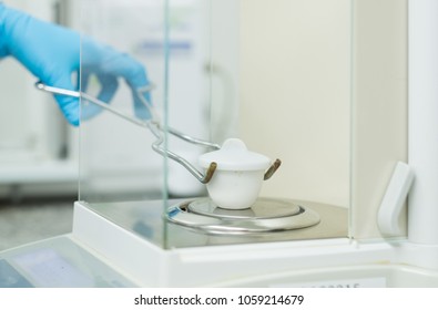 The operator is weighing the sample in the porcelain crucible for residue on ignition testing on the analytical balance in the laboratory, concept of qc testing activity in pharmaceutical industry.