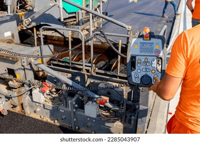 Operator, worker is holding industrial remote control, console with joystick to directing asphalt spreading machine, determines position for pouring, laying tarmac in right direction - Powered by Shutterstock