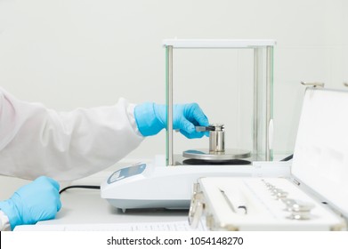 The operator's hand is holding stainless steel calibration weight to place on the analytical balance pan for the calibration test, concept of quality control laboratory in pharmaceutical industry.