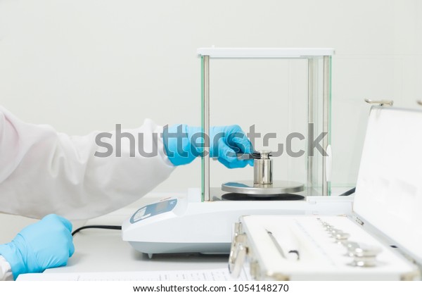 The operator\'s hand is holding stainless steel\
calibration weight to place on the analytical balance pan for the\
calibration test, concept of quality control laboratory in\
pharmaceutical industry.