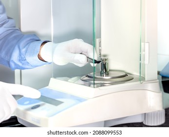 A operator's hand is holding steel calibration weight to place on the analytical balance. Concept of quality control in a laboratory.