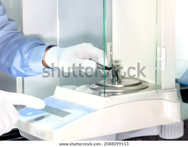 A operator\'s hand is holding steel\
calibration weight to place on the analytical balance. Concept of\
quality control in a\
laboratory.