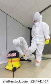 Operators in type 5-6 hazmat suits mutually performing decontamination procedure with high efficiency vacuum cleaner, after asbestos incident - Shutterstock ID 2244741467