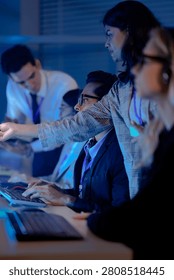 Operators wearing headsets work at computers in a dark modern call center monitoring data on glowing screens at night.