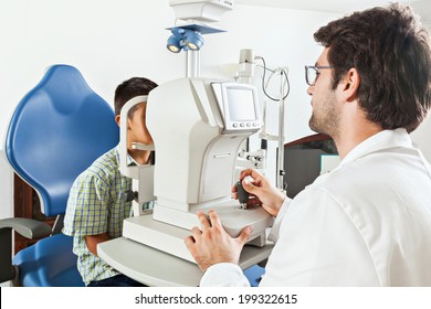 Ophthalmologist In Exam Room With Little Boy Sitting In Chair Looking Into Eye Test Machine