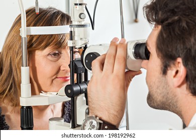 Ophthalmologist In Exam Room With Mature Woman Sitting In Chair Looking Into Eye Test Machine