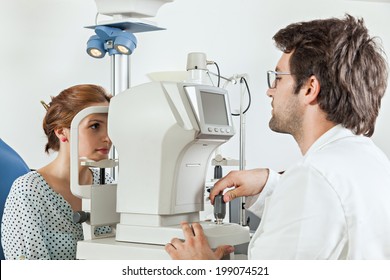 Ophthalmologist In Exam Room With Young Woman Sitting In Chair Looking Into Eye Test Machine