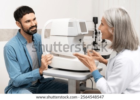 Ophthalmologist explaining the use of an autorefractor device to a male patient during an eye exam in a bright, modern ophthalmology clinic, focusing on eye health and vision care