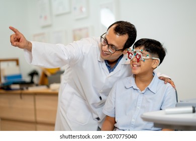 Ophthalmologist or optical staff point to the direction for viewing of Indian boy who wear special glasses to test his eye during process of eyecare in the shop.