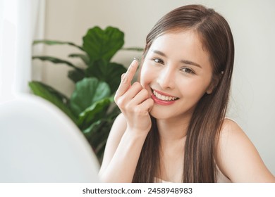 Ophthalmology care, eyesight or vision. Asian young woman, girl hand holding, wearing soft, daily disposable contact lens on her face with finger, looking in mirror at home. Medical and health care. - Powered by Shutterstock