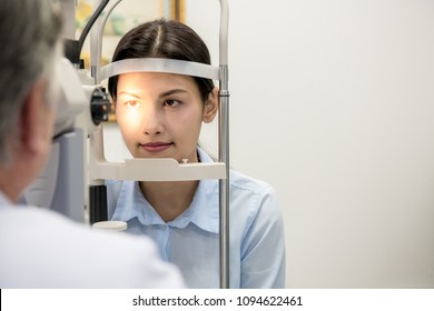 Opitcian with patient. Senior chinese optician with his asian woman patient in Optician room examine her eye. Real optician room in hospital. Medical concept.
