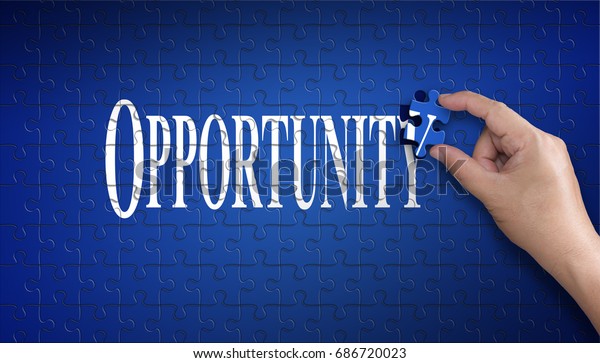 Opportunity word on Jigsaw puzzle - business\
concept. Man hand holding a blue puzzle to complete the Opportunity\
word divided over them concept of solution to a problem, challenge,\
plan and strategy.