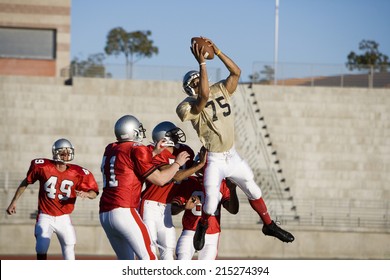 Opposing American football players competing for ball during competitive game, offensive receiver catching ball in mid-air - Powered by Shutterstock