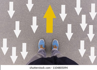 Opposing direction arrows on asphalt ground, feet and shoes on floor, personal perspective footsie concept for finding your own way - Shutterstock ID 1104805094