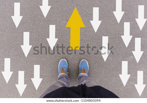 Opposing direction arrows on asphalt ground, feet and\
shoes on floor, personal perspective footsie concept for finding\
your own way