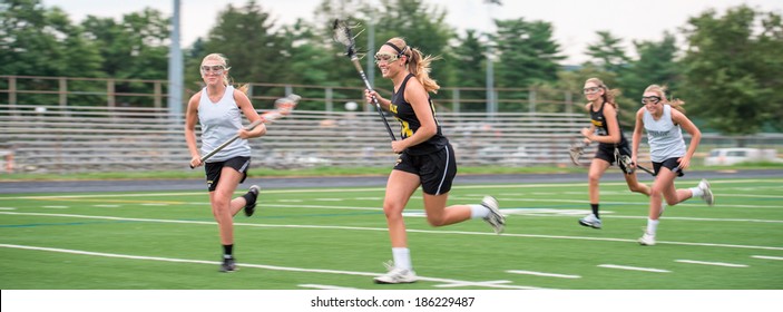 Opposing Teams Doing Battle During A Girls Lacrosse Game, Outdoors On Playing Field.