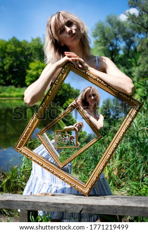 Optical illusion. The composition of an infinite image in a picture. A girl with blond hair on the lake shore holds a picture with an infinite image. A picture within a picture.